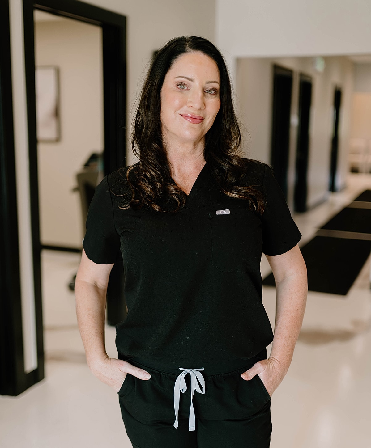 Smiling woman in black scrubs, hands in pockets.