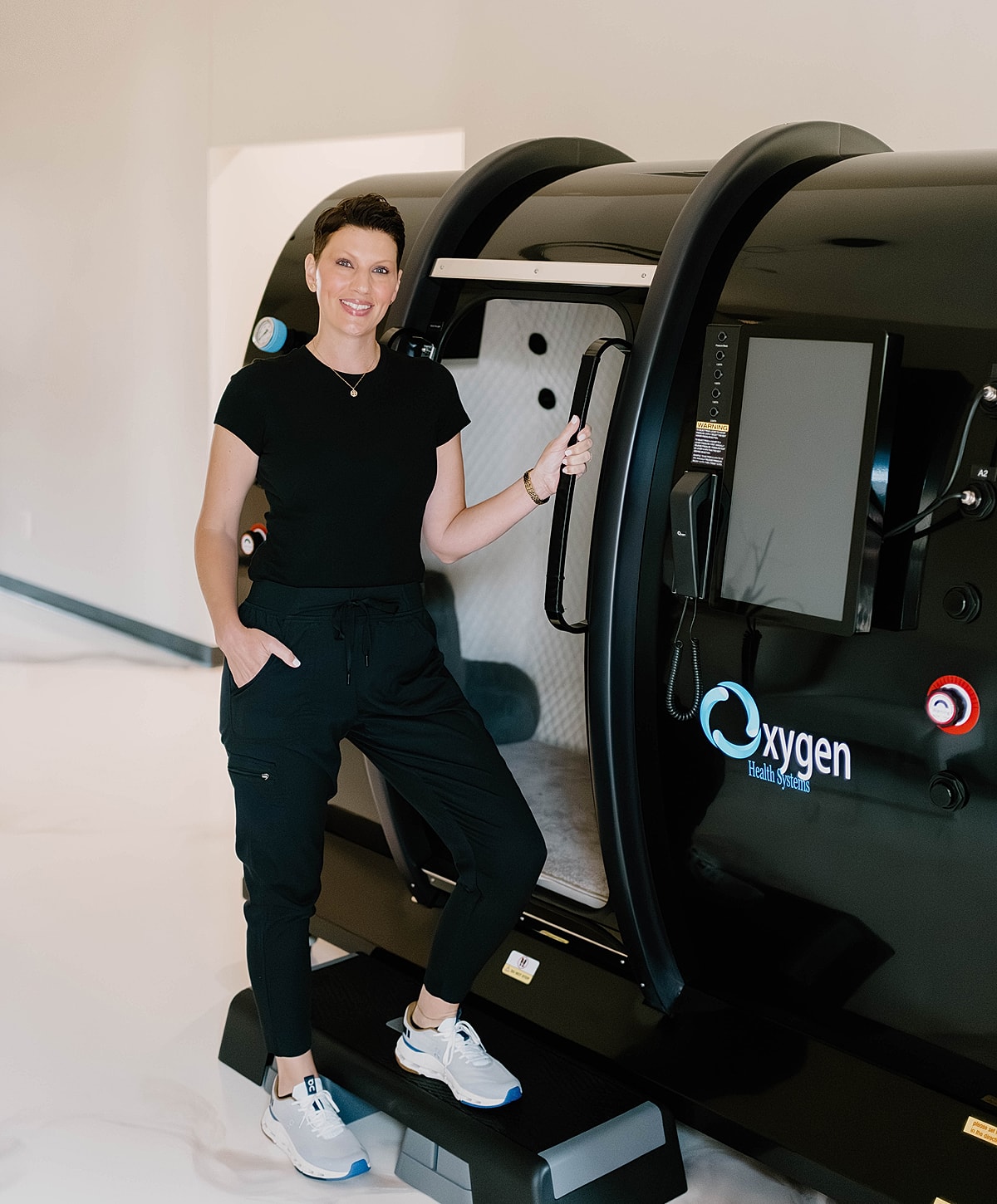 Woman beside a high-tech oxygen therapy chamber.