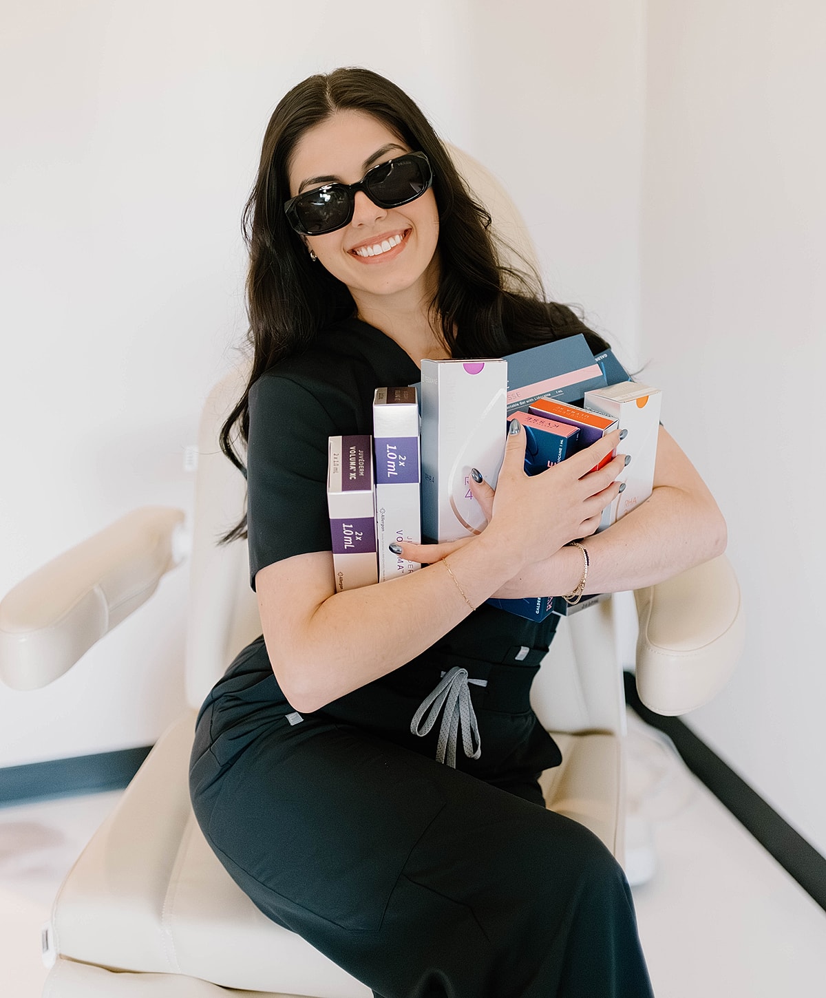 Woman in scrubs holding skincare products and smiling.