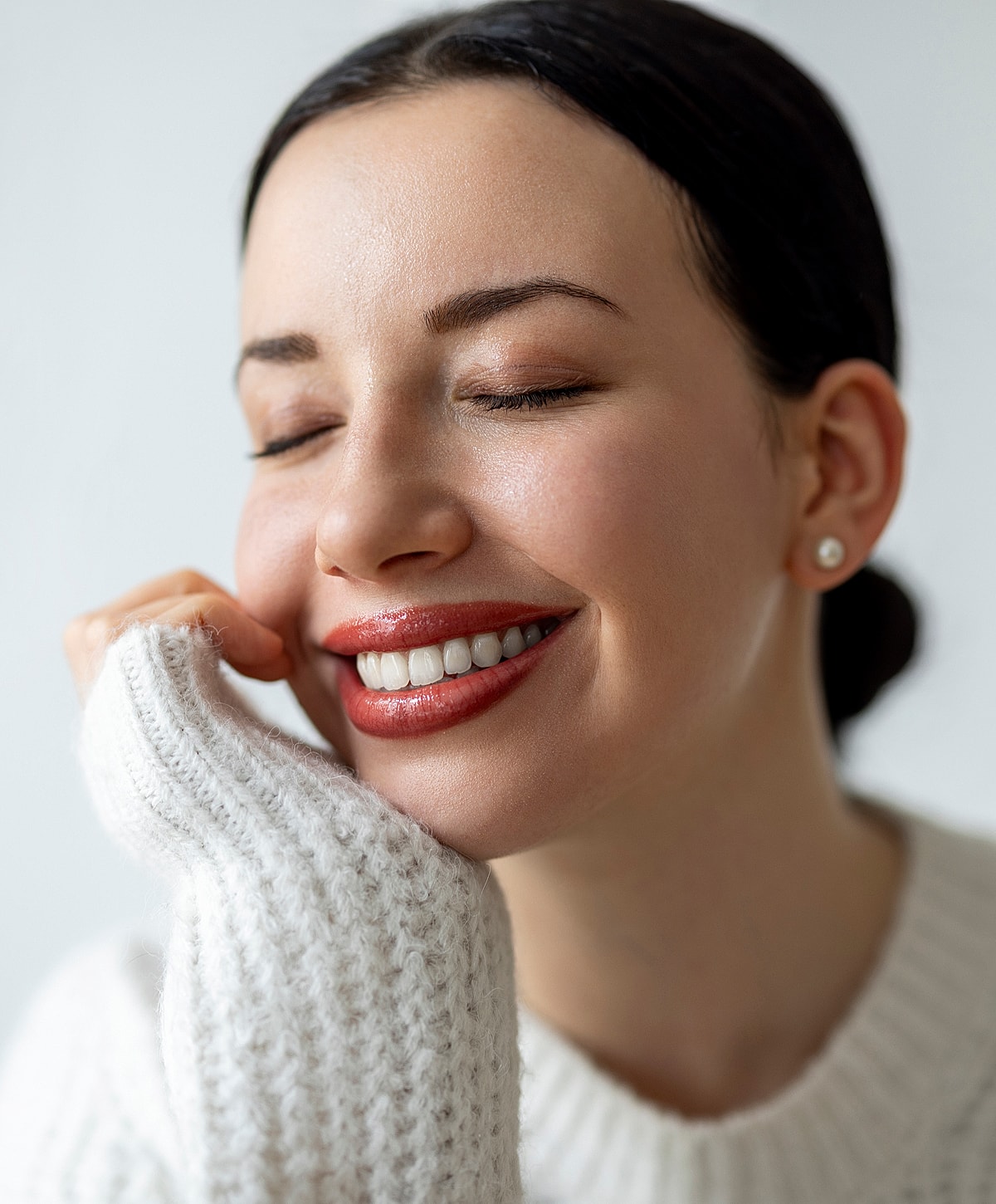 Smiling woman in cozy sweater, eyes closed.