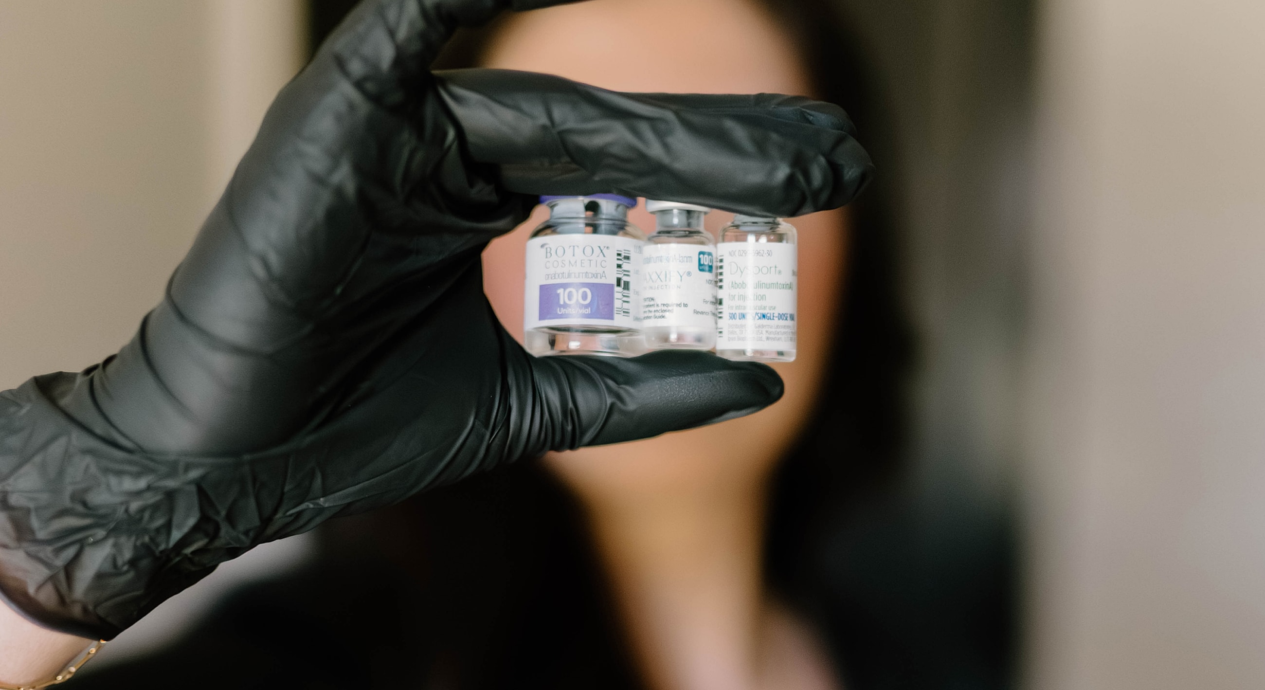Hand holding multiple Botox vials in gloves.