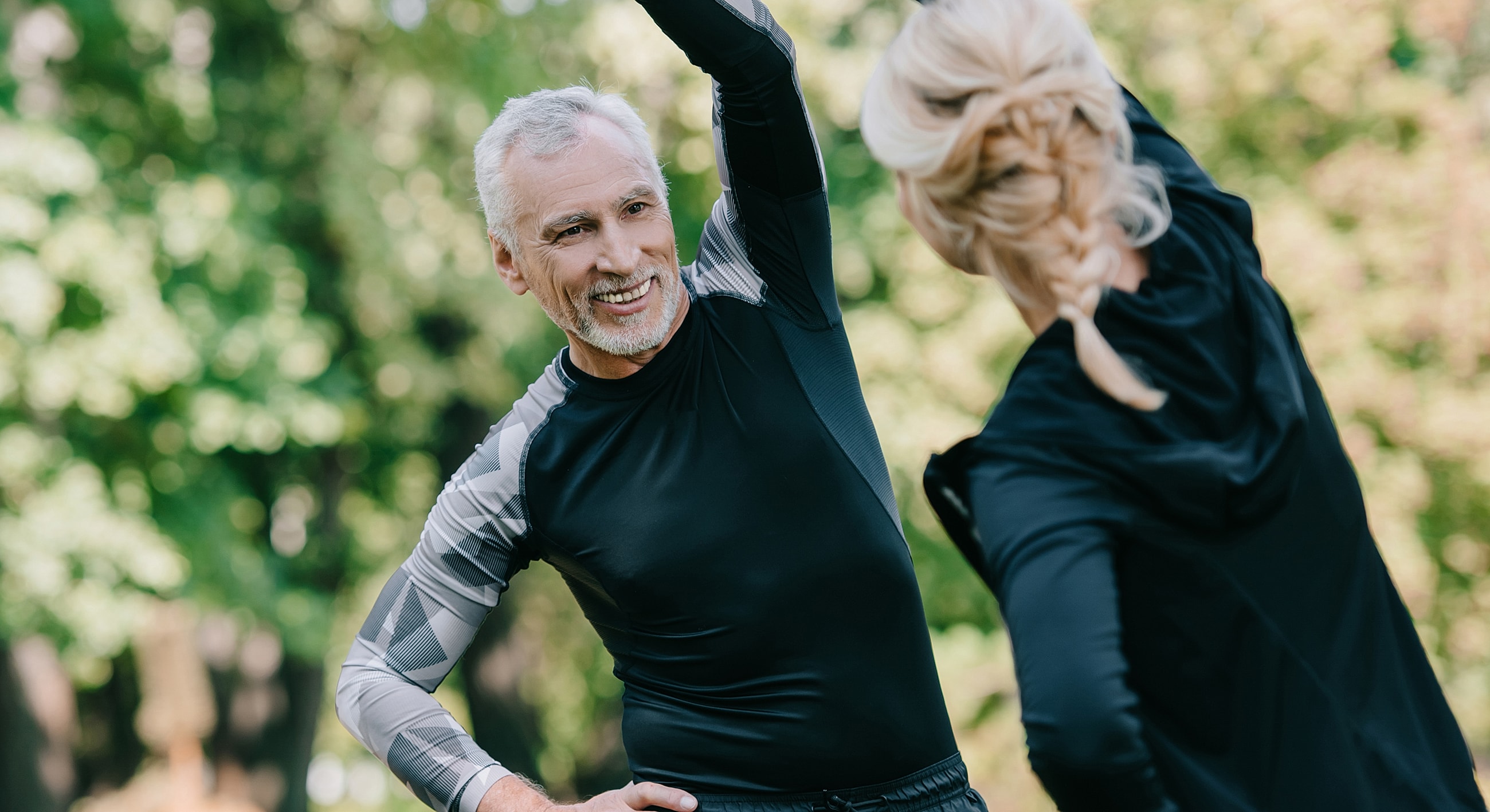 Two people stretching outdoors, smiling and interacting.